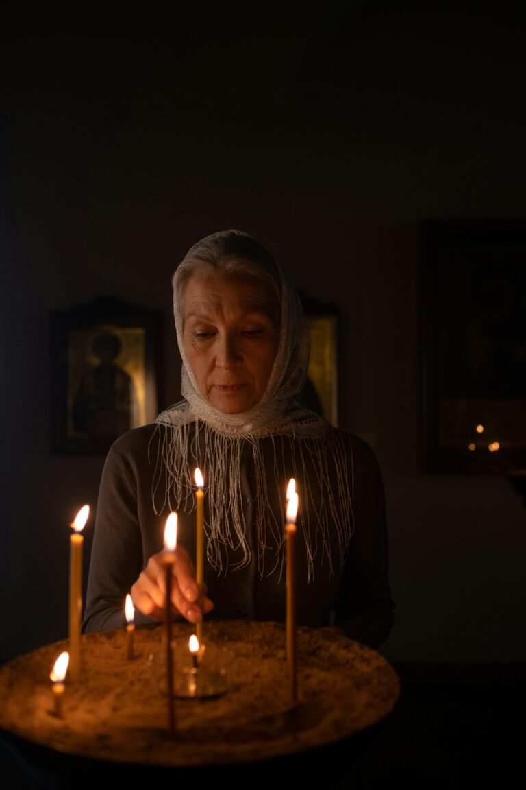 An elderly woman with a headscarf lights candles in a dimly lit room, creating a serene atmosphere.