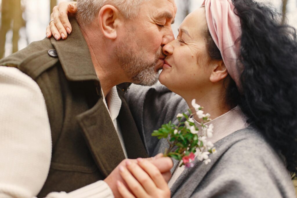 Elderly couple sharing a loving moment outdoors with a soft kiss.